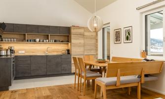 A modern kitchen with wooden shelves and a cozy dining table. The room has light walls and large windows that let in light.