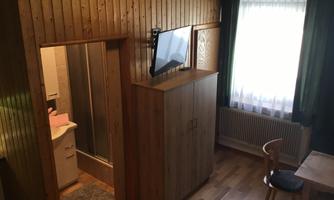 A cozy room with wooden paneling and a television. The room has a large window and a table with a chair.