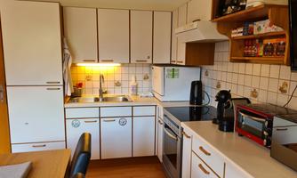 A modern kitchen with white cabinets and work surfaces. It is equipped with a stove, a microwave, and various kitchen appliances.