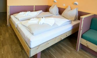 A modern room with two beds, outfitted with white bedding and towel-like decorations. The walls are painted in soft colors, and a cozy armchair is in the corner.
