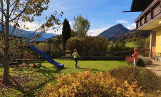 A beautiful garden with a slide and colorful balls. Children are playing outside in front of a picturesque mountain landscape.