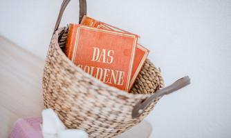 A woven basket with orange books that bear the title "DAS GOLDENE." The basket is on a light table.