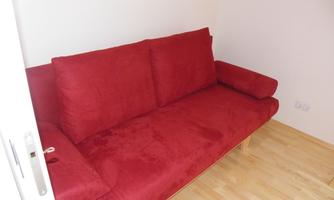 A red sofa with comfortable cushions is in a bright room. The floor is made of light wood.