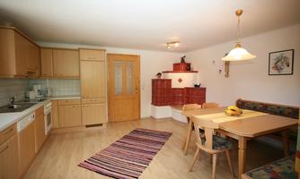 A bright kitchen with wooden cabinets and a dining table. The room is cozily furnished and has a colorful runner on the floor.