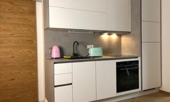 A modern kitchen unit with gray front panels and white cabinets. A pink kettle and an aqua-colored toaster add a colorful accent.