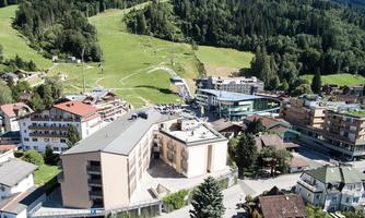 A picturesque landscape with hills and forests. In the foreground, buildings and streets of a small town are visible.