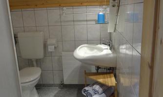 A small bathroom with wooden walls. There is a shower, a sink, and towels on a shelf.