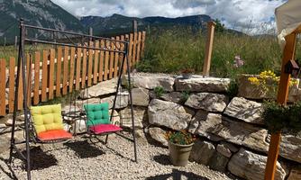 A cozy swing bench with colorful cushions in a picturesque setting. In the background, mountains and a natural garden can be seen.