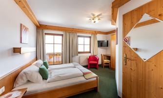 A cozy bedroom with a double bed and two pillows. The room has large windows, a television, and an inviting sitting area.