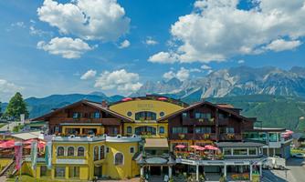 A picturesque building in the mountains, surrounded by a clear sky and gentle clouds. The view displays an inviting atmosphere with flowers and terraces.