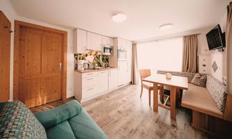 A modern, bright kitchen with a dining area and a cozy sofa. Large windows provide plenty of natural light.