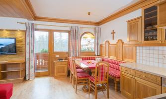 A cozy kitchen with wooden paneling and a large dining table. A TV hangs on the wall and the windows provide a view outside.