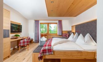 A modern hotel room with two beds and wooden details. The room has large windows with a view of greenery and a cozy decor.