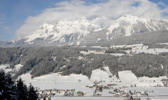 A winter landscape with snow-covered mountains in the background. In the foreground, snowy meadows and small villages can be seen.