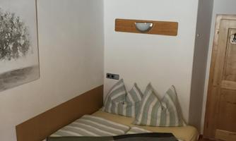 A cozy bedroom with a double bed and striped pillows. There is a wooden floor and a simple, light decor.