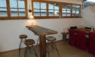 A modern kitchen with a large dining table and wooden bar stools. Large windows provide plenty of daylight and a cozy atmosphere.