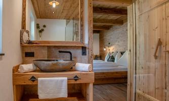 A modern bathroom with wooden details and a stylish sink. In the background, a cozy bedroom is visible.