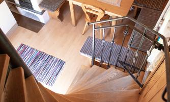 A cozy room with a wooden table, chairs, and a wood stove. The staircase leads downstairs and the floor is made of warm wood.