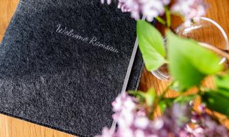 A stylish notebook with the inscription "Welcome" lies on a wooden surface. Next to it, fresh purple flowers bloom in a vase.