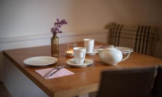 A beautifully set table with a teapot, cups, and plates. A flower vase and a candlelight create a cozy atmosphere.