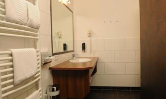 A modern bathroom with a mirror, a sink, and a towel rack. The walls are brightly tiled, and there is a metal trash can.