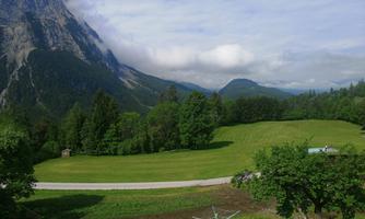 An idyllic landscape with green meadows and majestic mountains in the background. The sky is clear with a few clouds.