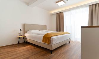 A modern bedroom with a large bed and a yellow throw. The calm colors and large windows create a bright and inviting atmosphere.