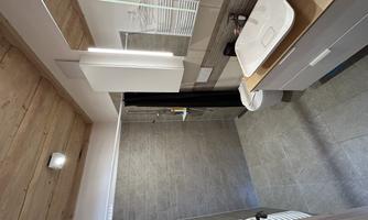 A modern bathroom with a shower and a sink on a wooden shelf. The walls are in neutral colors and the ceiling has wood paneling.
