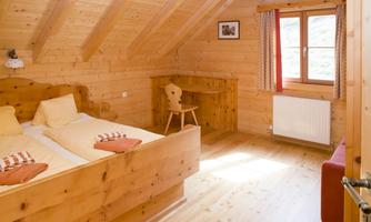 A cozy wooden room with two beds and a desk. Large windows allow plenty of daylight in.