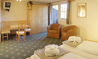 A cozy room with two beds, a table, and chairs. There is a television and large windows that provide plenty of light.