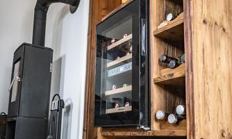 A stylish wooden wine cabinet with a glass door that showcases several bottles. In the background, there is a fireplace and a television.