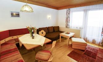 A cozy living area with a dining space, a couch, and a table. The walls are bright and adorned with window decorations.