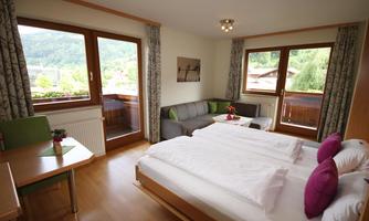 A cozy hotel room with two beds and a sofa bed. Large windows offer a view of the landscape.