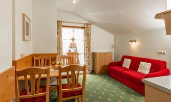 A cozy living space with a red sofa and a dining table. Large windows provide plenty of daylight and a view outside.