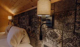 A cozy bedroom with two pillows and a decorative wall lamp. The walls are designed with a beautiful pattern and wood paneling.