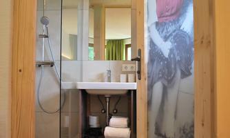 A modern bathroom with a glass shower cabin and a simple sink. On the wall, there is a picture of a person in a red top.