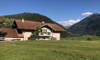 A large house in a picturesque landscape with gentle hills and mountains in the background. The sky is blue with some clouds.