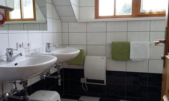 A modern bathroom with two sinks and large windows. The walls are tiled and there are fresh towels in green color.