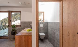 A modern bathroom with wood and gray tones. Large windows provide a view of the mountains.