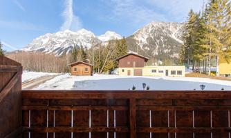 A picturesque winter landscape with snow-covered mountains in the background. In the foreground, there are cozy wooden houses and coniferous trees.