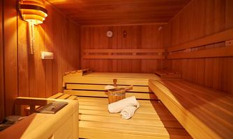 A cozy sauna with a wooden bench and soft lighting. In the room, there is a towel and a bucket of water.