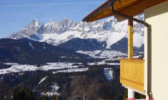 A picturesque mountain landscape with snow-capped peaks. In the foreground, a wooden balcony is visible.