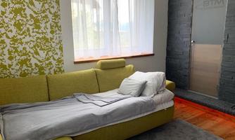 A cozy living room with a yellow sofa, white bedding, and large windows. The wall is decorated with a striking pattern.