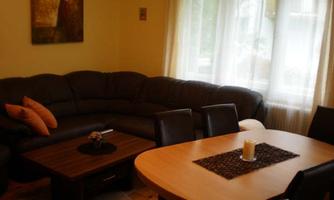 A cozy living room with a large, dark gray couch and a round table. Large windows let in a lot of daylight.