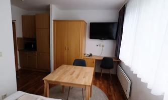 A bright and modern apartment with a table, chairs, and a television. In the background, kitchen cabinets and a large window can be seen.