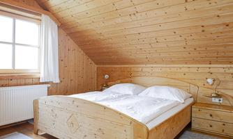 A cozy bedroom with wooden paneling and a double bed. The window lets in plenty of light and creates an inviting atmosphere.