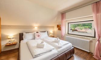 A cozy bedroom with a double bed and large windows. Soft colors and decorative elements create an inviting atmosphere.