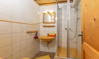 A small bathroom with a shower cabin and a sink. The walls are tiled and there is a wooden ceiling.