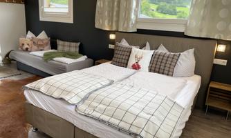 A cozy bedroom with a large bed and an additional sofa bed. Soft bedding and decorative cushions give the room an inviting atmosphere.