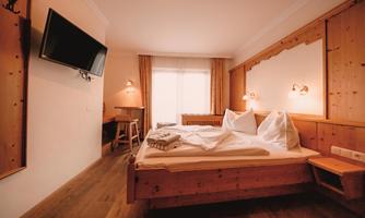 A cozy room with a double bed and wooden furniture. The room features a television and plenty of daylight.
